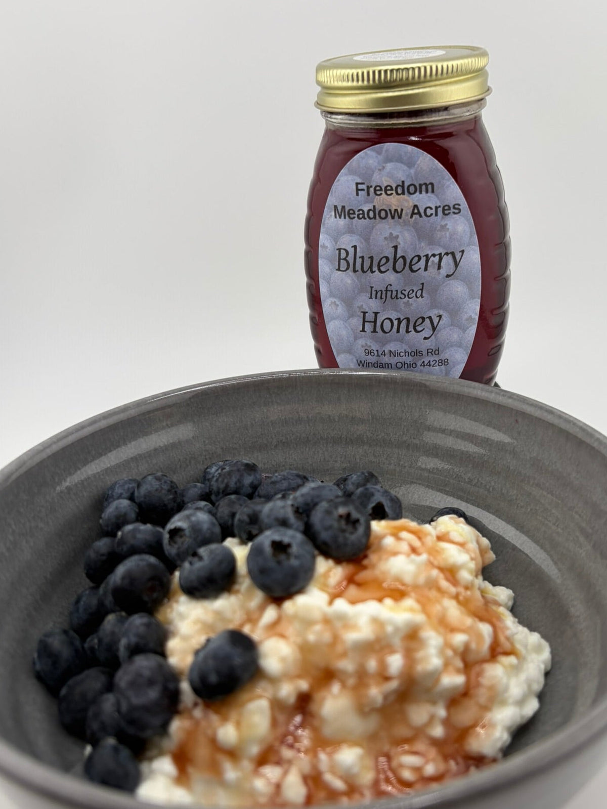 A gray ceramic bowl filled with creamy cottage cheese topped with fresh blueberries and drizzled of blueberry infused honey.